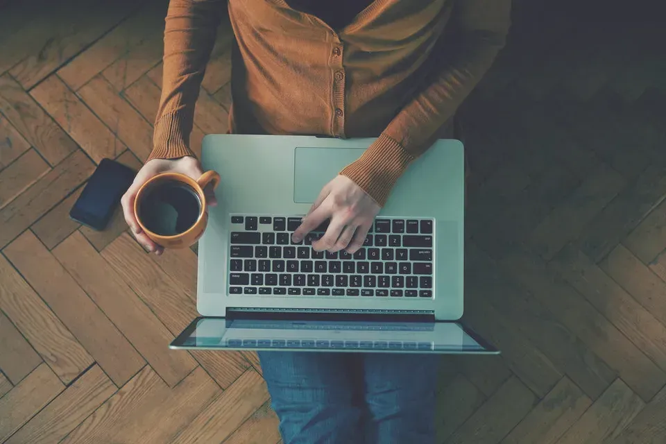 Person using laptop with coffee sitting on the floor.